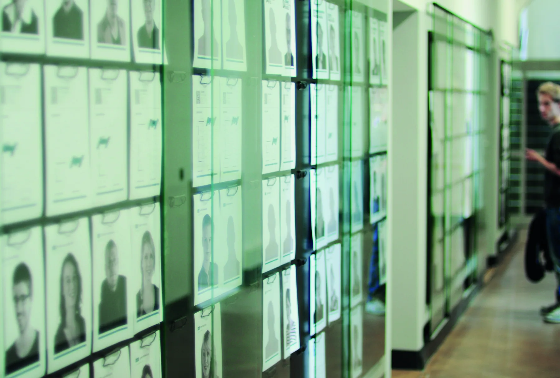 Exhibition: rows of printed portraits behind green-tinted glass panels in a corridor